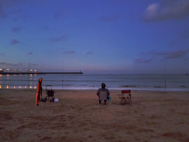 Photo rear view of man sitting on chair against sea at night