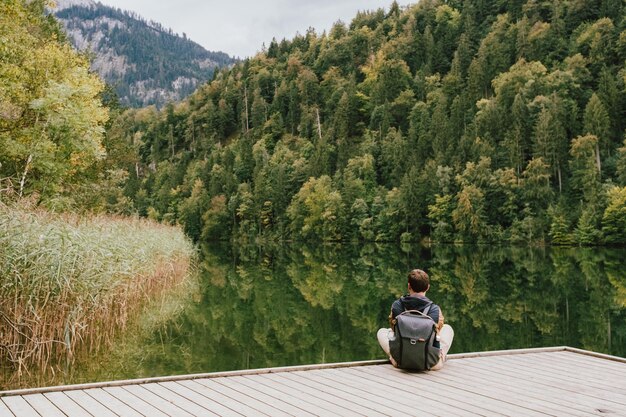 Photo rear view of man sitting on pier by lake against trees in forest