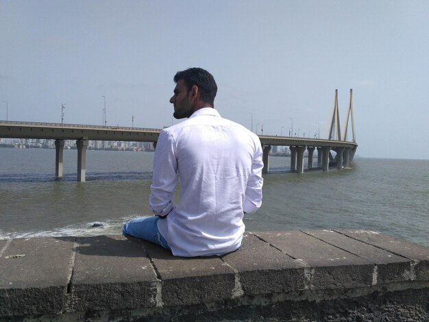 Rear view of man sitting on pier over sea