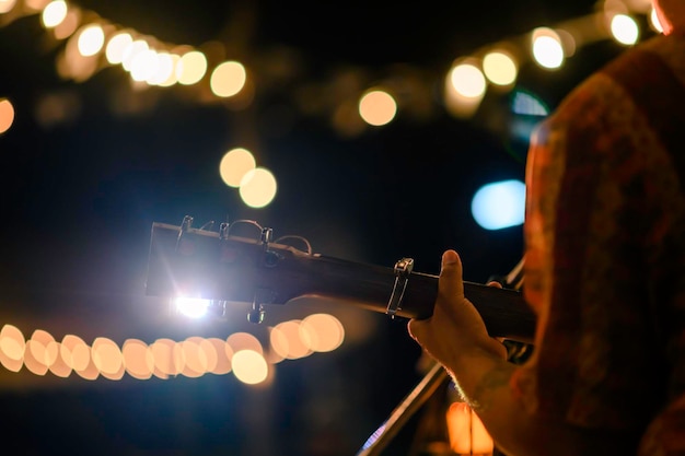 음악적 개념인 전면에 마이크 스탠드가 있는 야외 콘서트에서 어쿠스틱 기타를 연주하는 남자의 뒷모습.