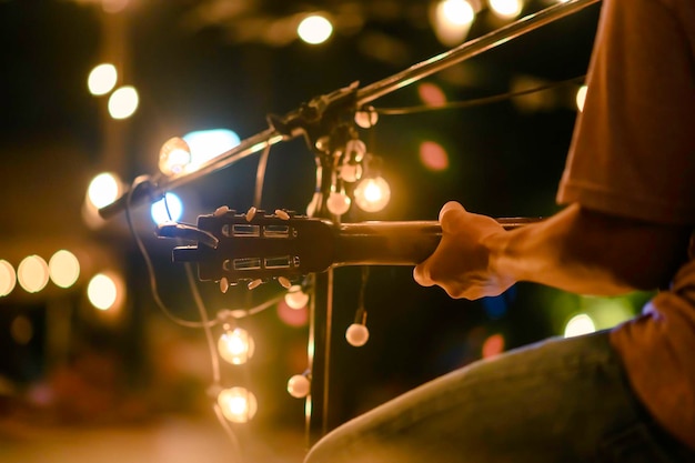 La vista posteriore dell'uomo seduto suona la chitarra acustica durante il concerto all'aperto con un supporto per microfono nella parte anteriore, concetto musicale.