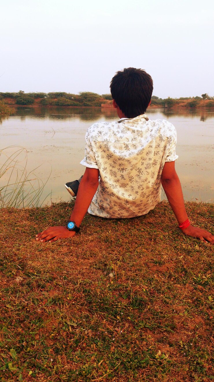 फोटो rear view of man sitting on riverbank against clear sky at sunset