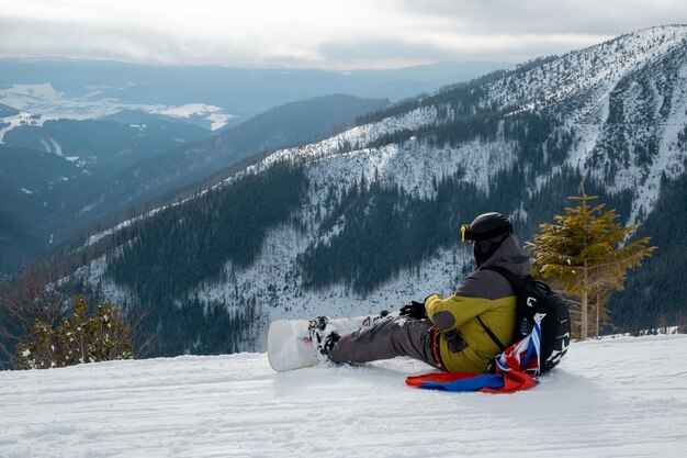 Photo rear view of man sitting on snowcapped mountain