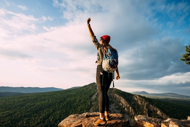 Rear view of a man standing against the background of a mountain with his hand raised. A man in the mountains raises his hand. A man on the background of mountains. A trip to the mountains. Copy space