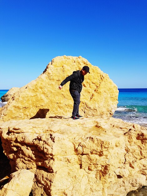 Rear view of man standing on beach against clear blue sky