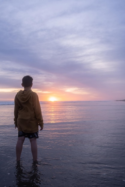 Foto vista posteriore di un uomo in piedi sulla spiaggia contro il cielo durante il tramonto