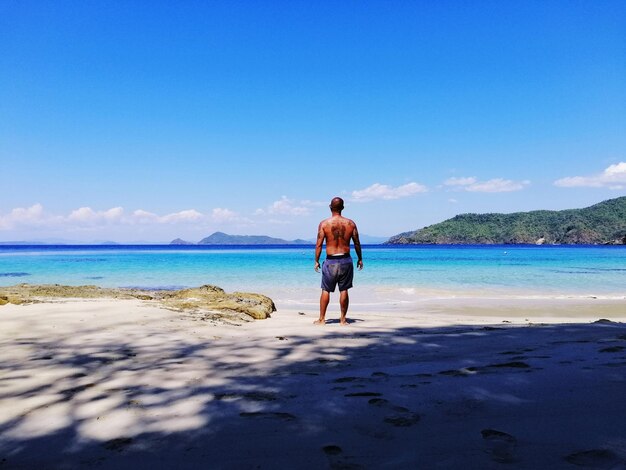 Rear view of man standing on beach against sky