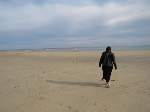 Rear view of man standing on beach against sky