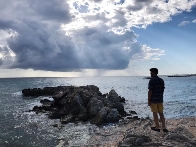 Foto vista posteriore di un uomo in piedi sulla spiaggia contro il cielo