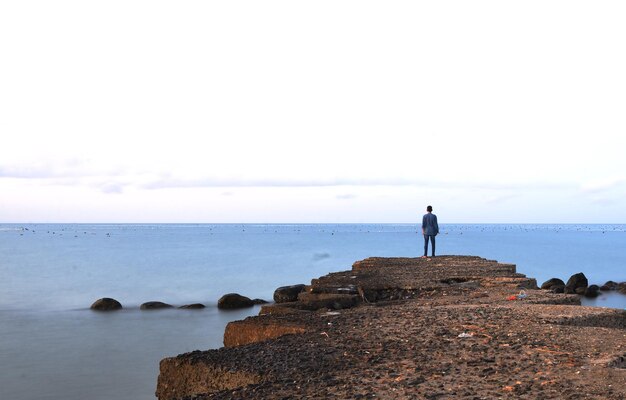 Foto vista posteriore di un uomo in piedi sulla spiaggia contro il cielo