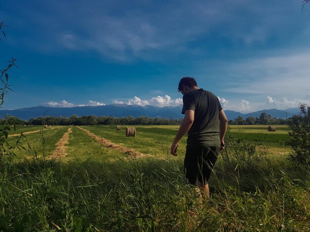 Rear view of man standing by plants in farm against sky