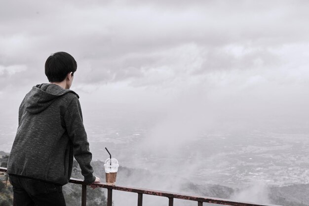 Rear view of man standing by railing against sky