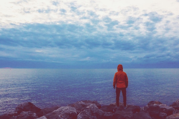 Foto vista posteriore di un uomo in piedi sul mare su una roccia