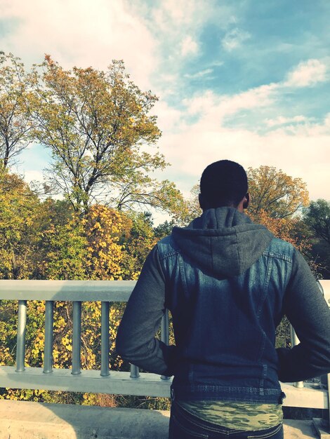 Photo rear view of man standing on footbridge by trees against cloudy sky