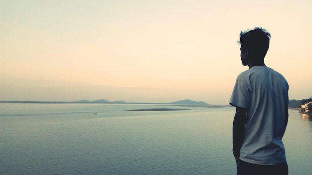Rear view of man standing in front of sea against sky