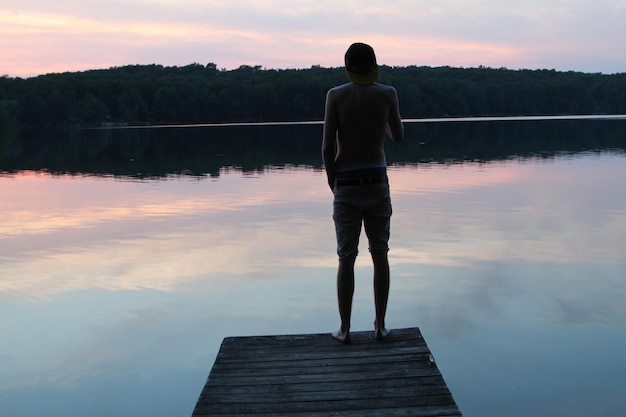 Foto vista posteriore di un uomo in piedi sul molo sopra il lago durante il tramonto