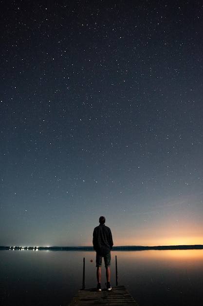 Foto vista posteriore di un uomo in piedi sul molo sopra il mare contro il cielo di notte