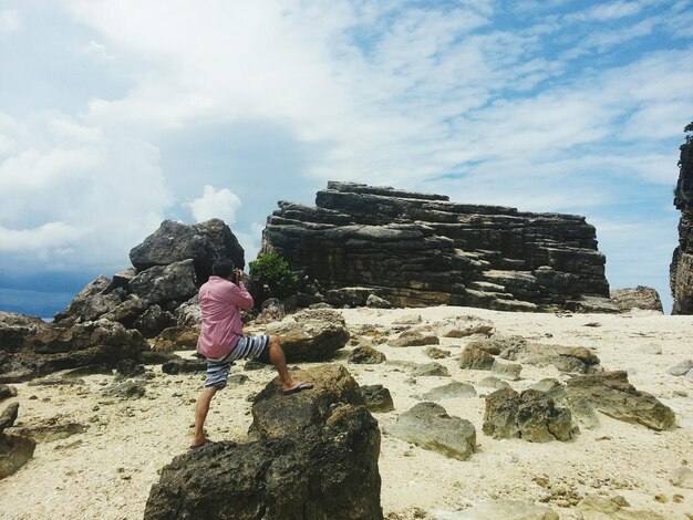 Rear view of man standing on rock against cloudy sky