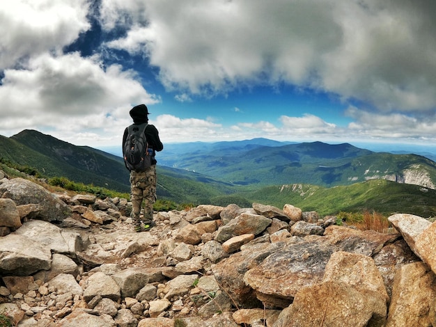 Rear view of man standing on rock against sky