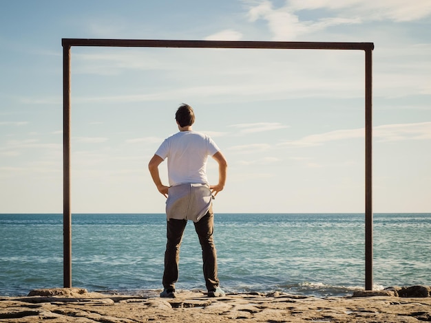 Photo rear view of man standing on rocky shore against sky