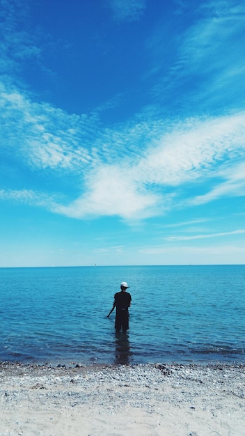 Rear view of man standing at sea against sky