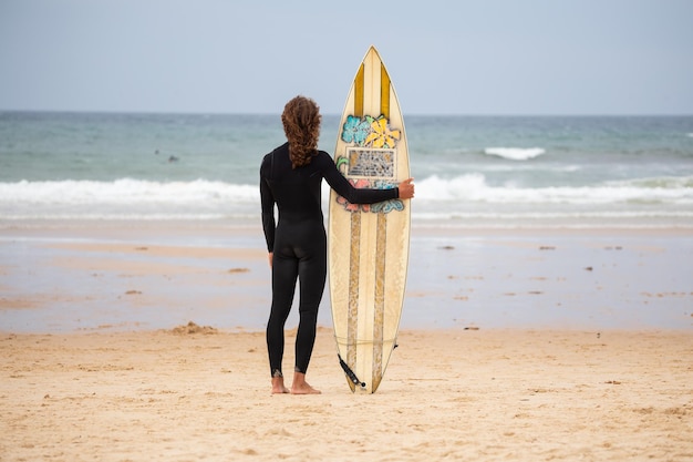 Photo rear view of man standing with surfboard at beach