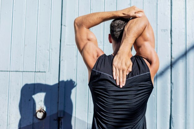 Photo rear view of man stretching while standing against wall