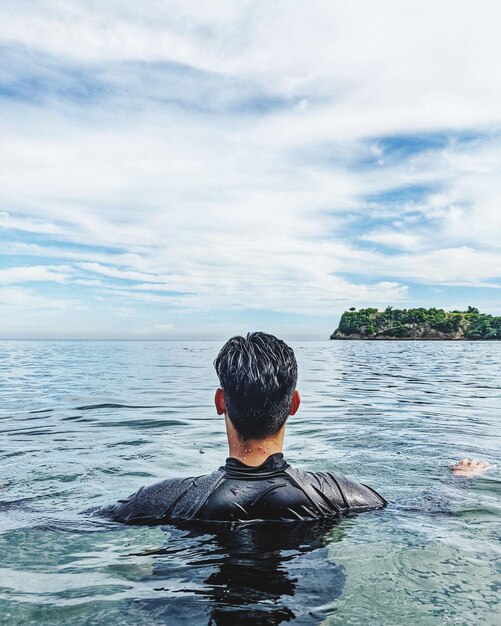 Rear view of man swimming in sea against sky