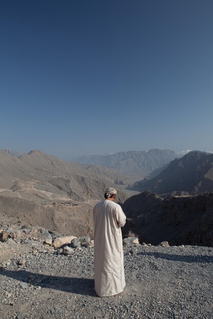Rear view of man in traditional clothing standing on mountain against clear sky