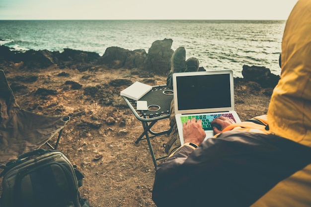 Photo rear view of man using laptop while sitting at beach against sea