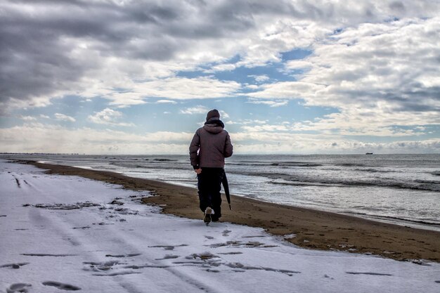 Rear view of man walking on beach during winter