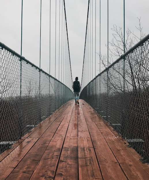 Foto vista posteriore di un uomo che cammina su un ponte pedonale contro il cielo