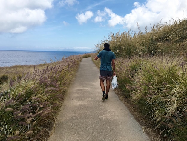 空の向こうの海で歩道を歩いている男の後ろの景色