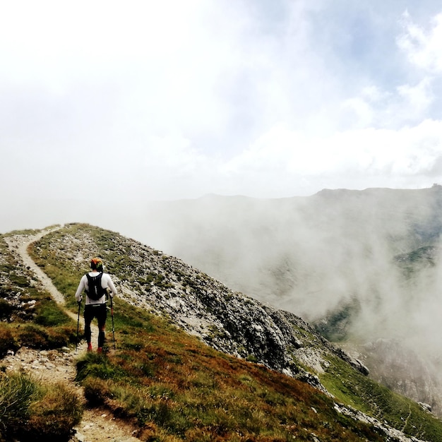 Rear view of man walking on mountain against sky