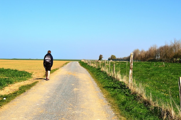 Rear view of man walking on road against clear blue sky