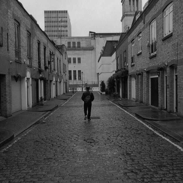 Photo rear view of man walking on road along buildings