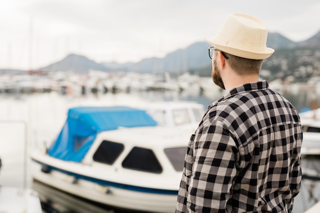 Rear view man wearing hat with yachts and marina background\
with copy space and empty place for advertising