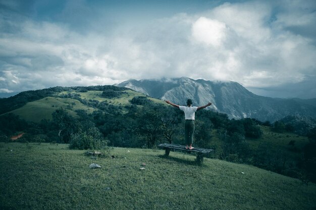 Photo rear view of man with arms outstretched standing on mountain against cloudy sky