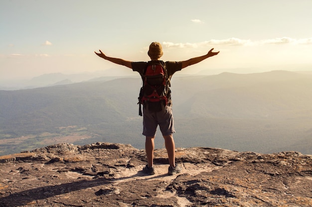 rear view of man with arms outstretched standing on mountain against sky