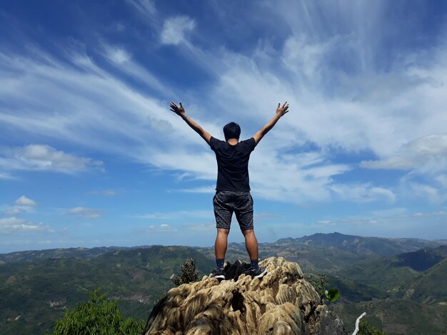 Foto vista posteriore di un uomo con le braccia alzate in piedi sulla montagna contro il cielo