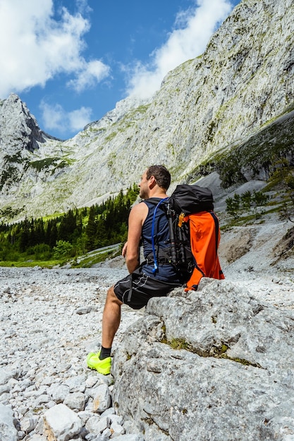 rear view of man with backpack sitting on rock