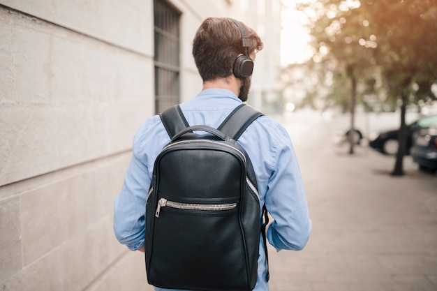 Rear view of a man with backpack walking on pavement