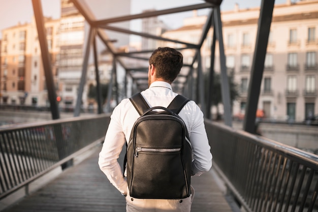 Вид сзади человека с черным рюкзаком, стоящим на мосту