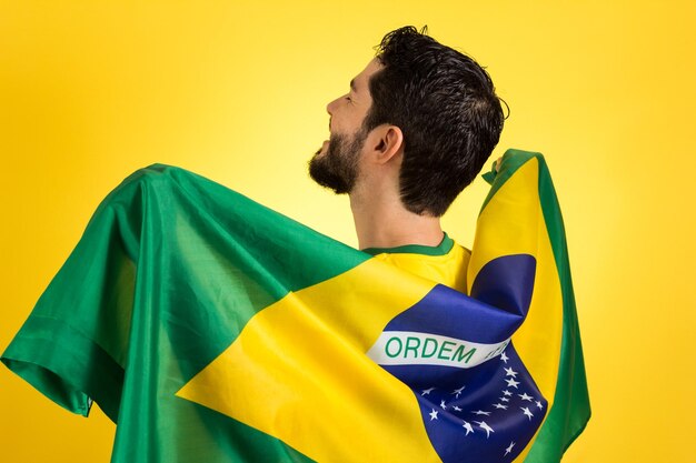 Photo rear view of man with brazil flag standing against yellow background