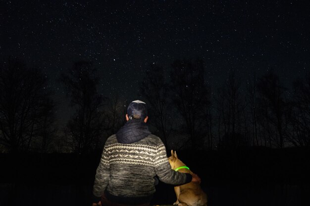 Photo rear view of man with dog in forest against star field at night