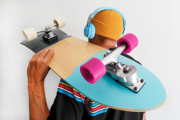 Foto vista posteriore dell'uomo con lo skateboard che indossa un cappello giallo che ascolta le cuffie wireless blu