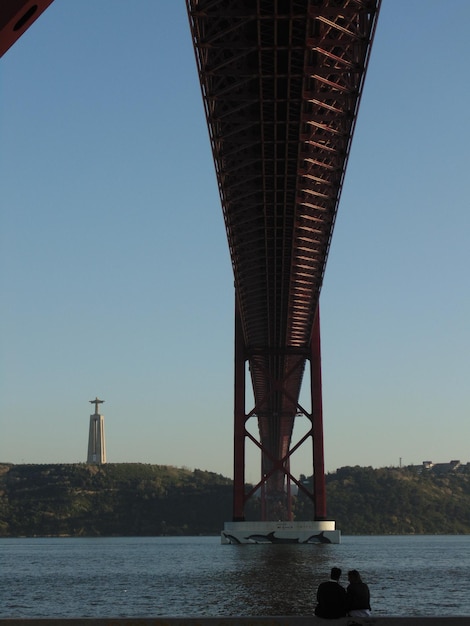 Foto vista posteriore di un uomo e una donna sotto il ponte del 25 aprile sul fiume tago