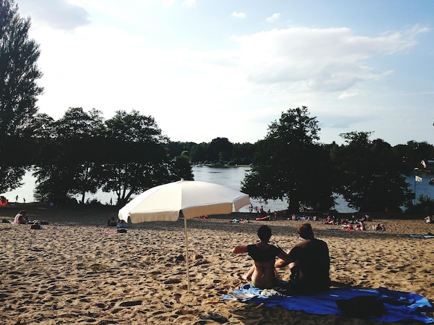 Photo rear view of man and woman sitting by sunshade on beach