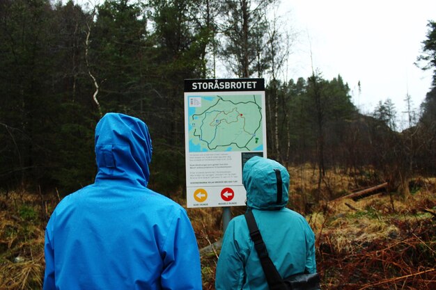 Rear view of man and woman standing by information sign in forest