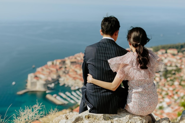 Rear view of married couple sitting on rock against sea